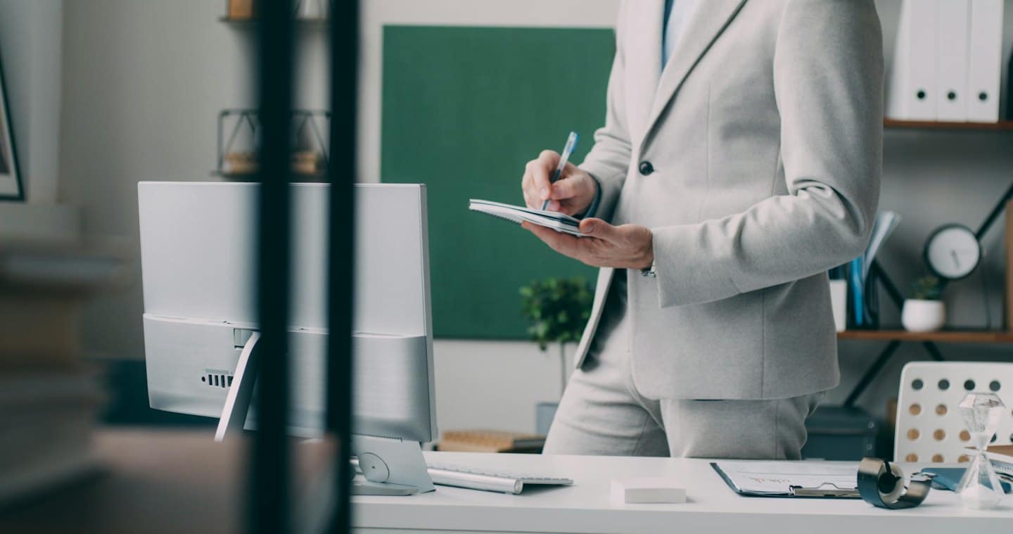 Person in a grey suit taking notes at an office desk.